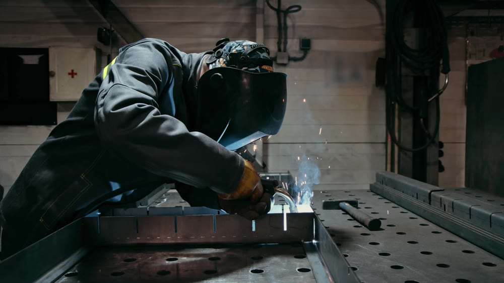 Workers in industrial uniform and welded iron mask in steel factories, first industrial safety concept. Slow motion in low light.
