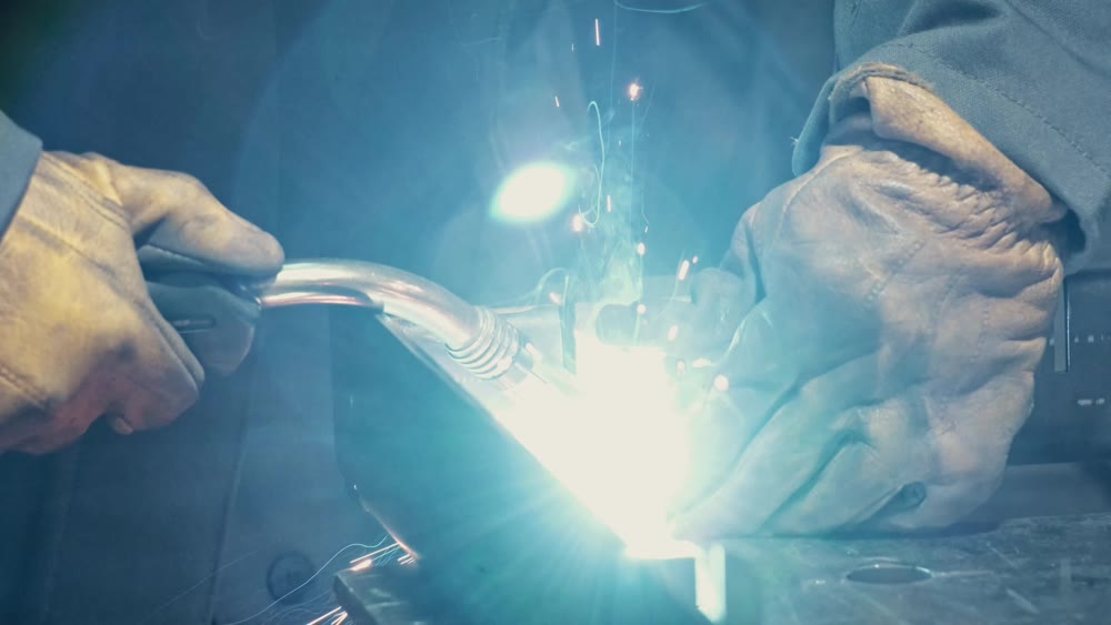 Close-up of a blacksmith welder working with metal using a welding machine, bright sparks and flashes in slow motion