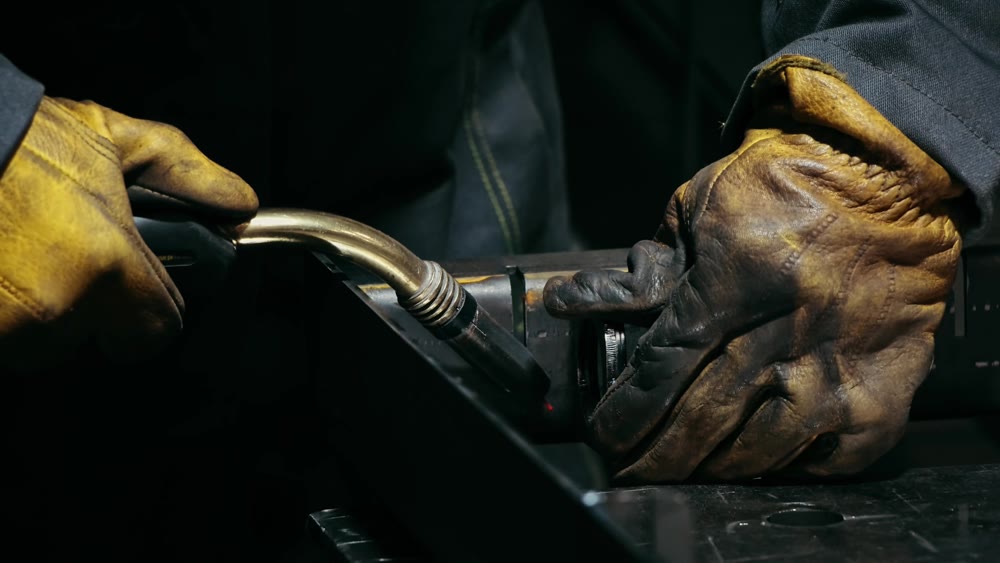 Close-up of a blacksmith welder working with metal using a welding machine, bright sparks and flashes in slow motion