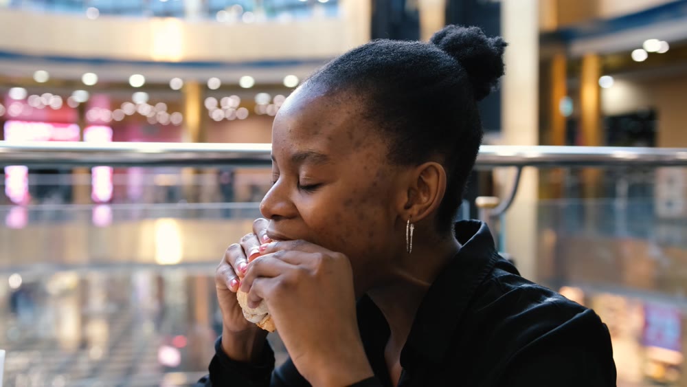 Young african american woman eating fast food in a restaurant enjoying delicious juicy burger