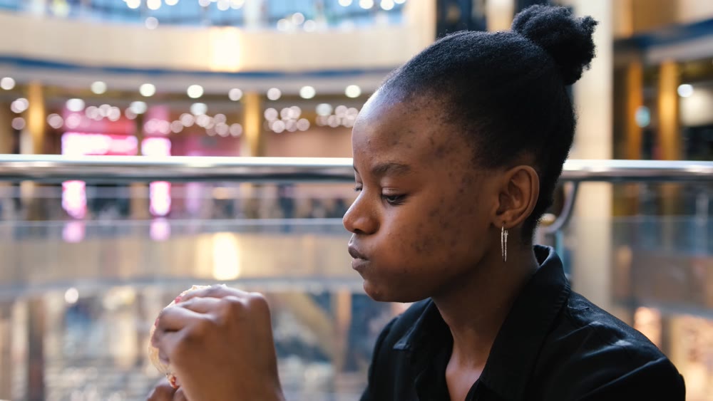 Young african american woman eating fast food in a restaurant enjoying delicious juicy burger