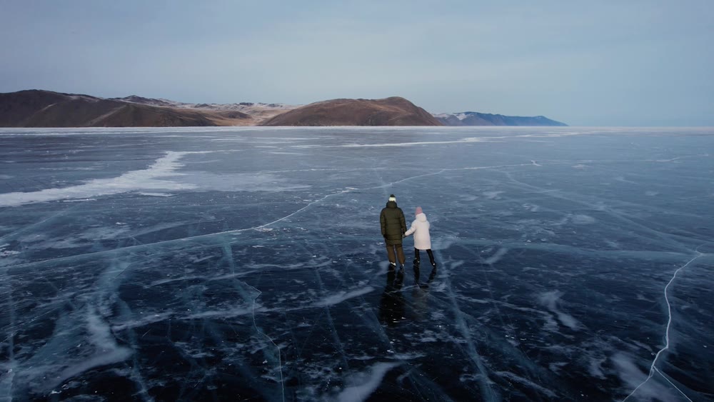A man-father with a little girl-daughter is skating on the blue transparent ice of the boundless Lake Baikal. Unique places on earth.