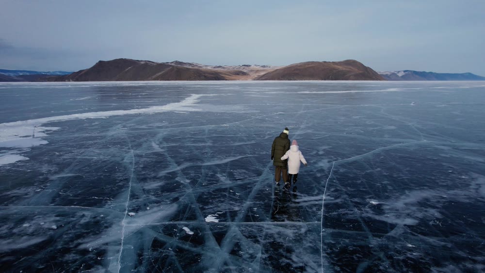 A man-father with a little girl-daughter is skating on the blue transparent ice of the boundless Lake Baikal. Unique places on earth.