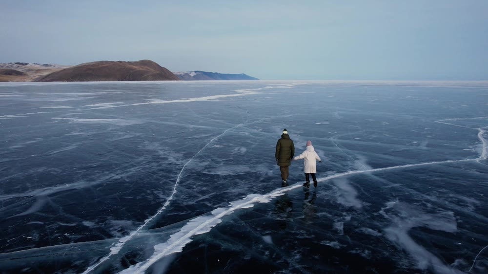 A man-father with a little girl-daughter is skating on the blue transparent ice of the boundless Lake Baikal. Unique places on earth.