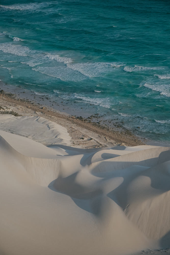 Gentle coastal scene. Peaceful dunes meet crashing waves. Calm sands and surf contrasted by distant horizon