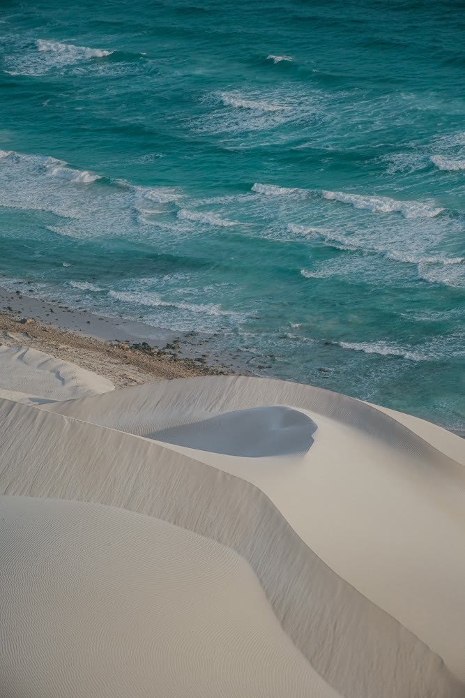 Smooth dunes meet tranquil waters. Graceful sand formations and gentle waves create soothing scenery