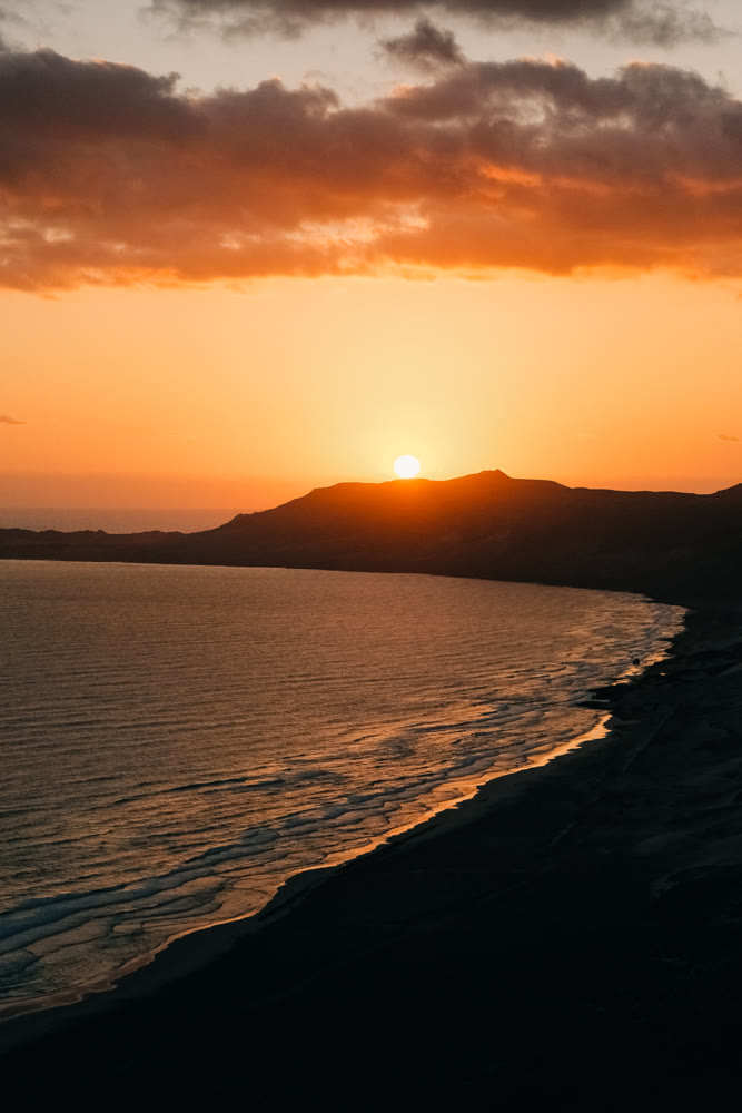 Vivid sunset with coastal silhouette. Dramatic dusk with layered clouds reflecting in calm waters