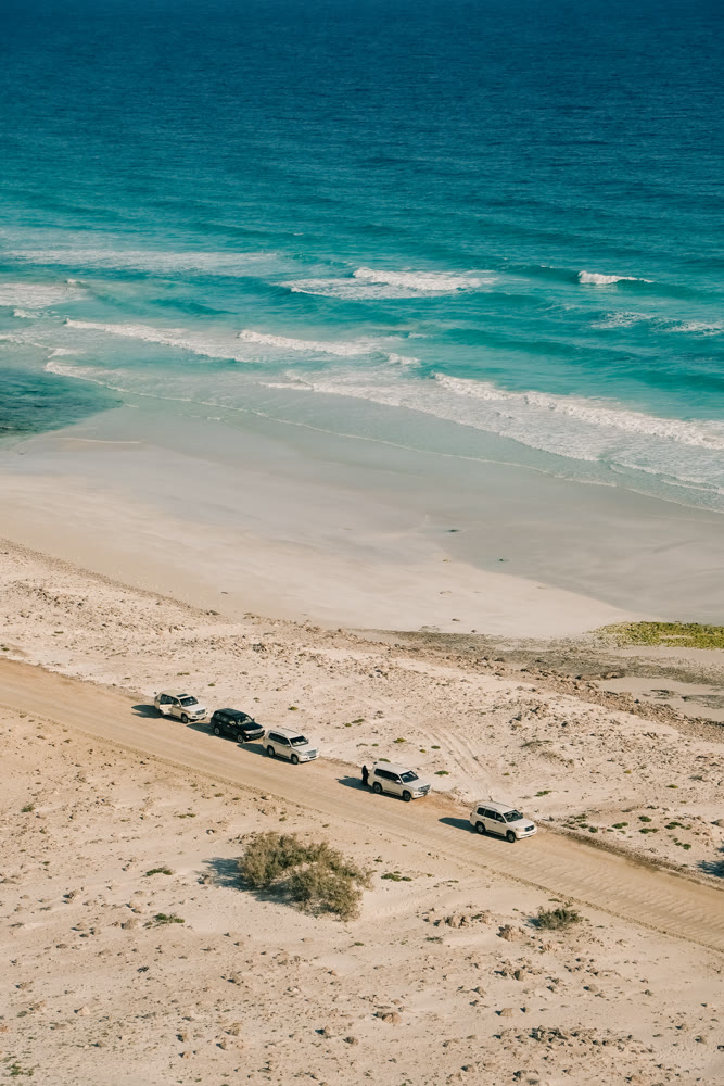 Exploration scene with offroad cars parked on dunes next to sparkling blue sea and sandy shoreline