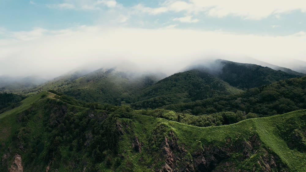 Verdant ridges beneath cloudy skies. Hazy mountains with lush plains and peaceful pathways stretch out